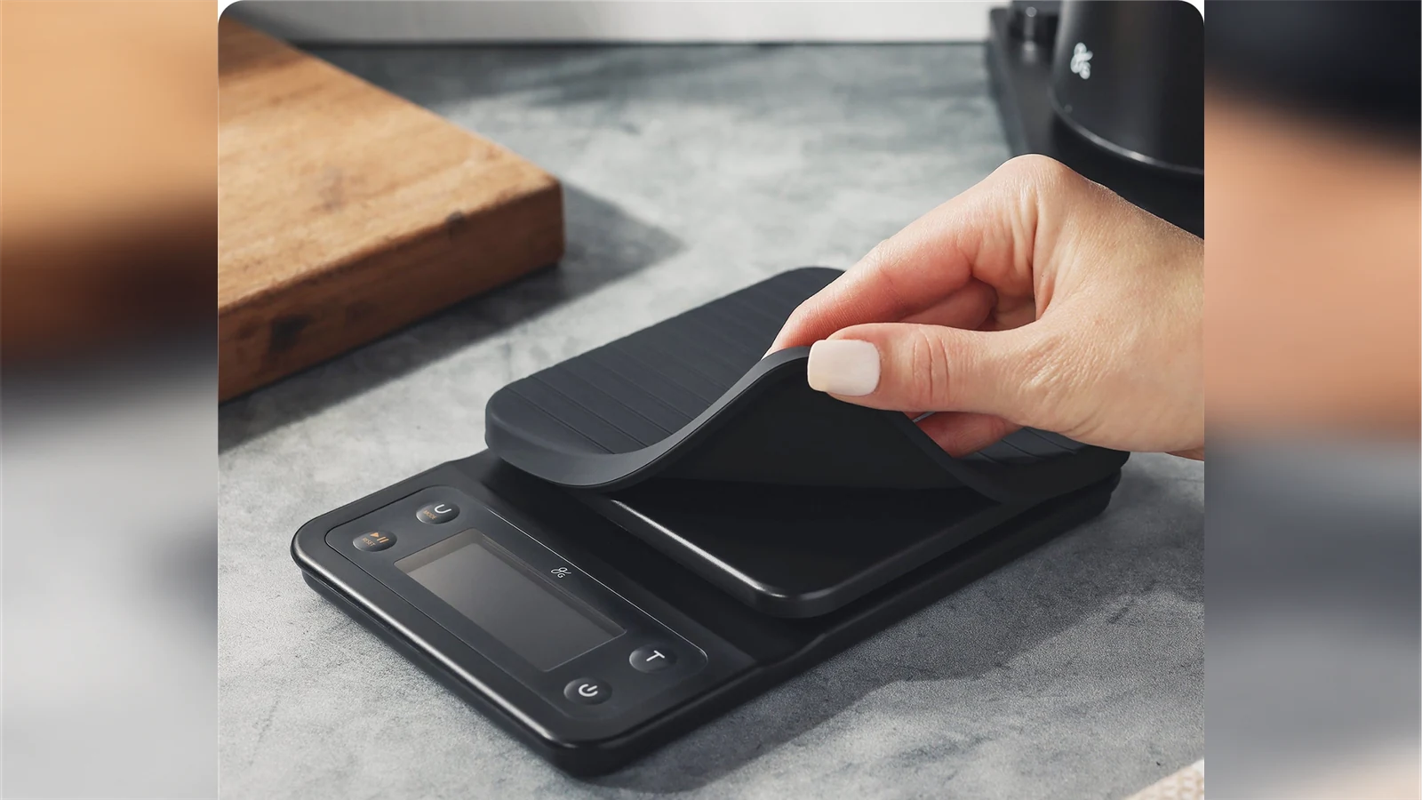 A hand lifting the removable silicone mat from a Greater Goods Premium coffee scale