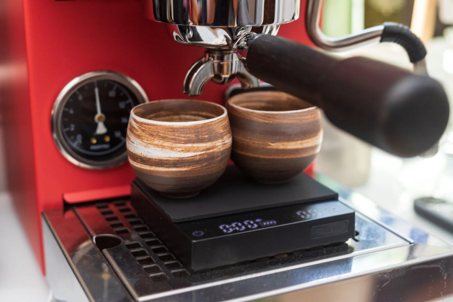 Two espresso cups on a compact coffee scale beneath a spouted portafilter