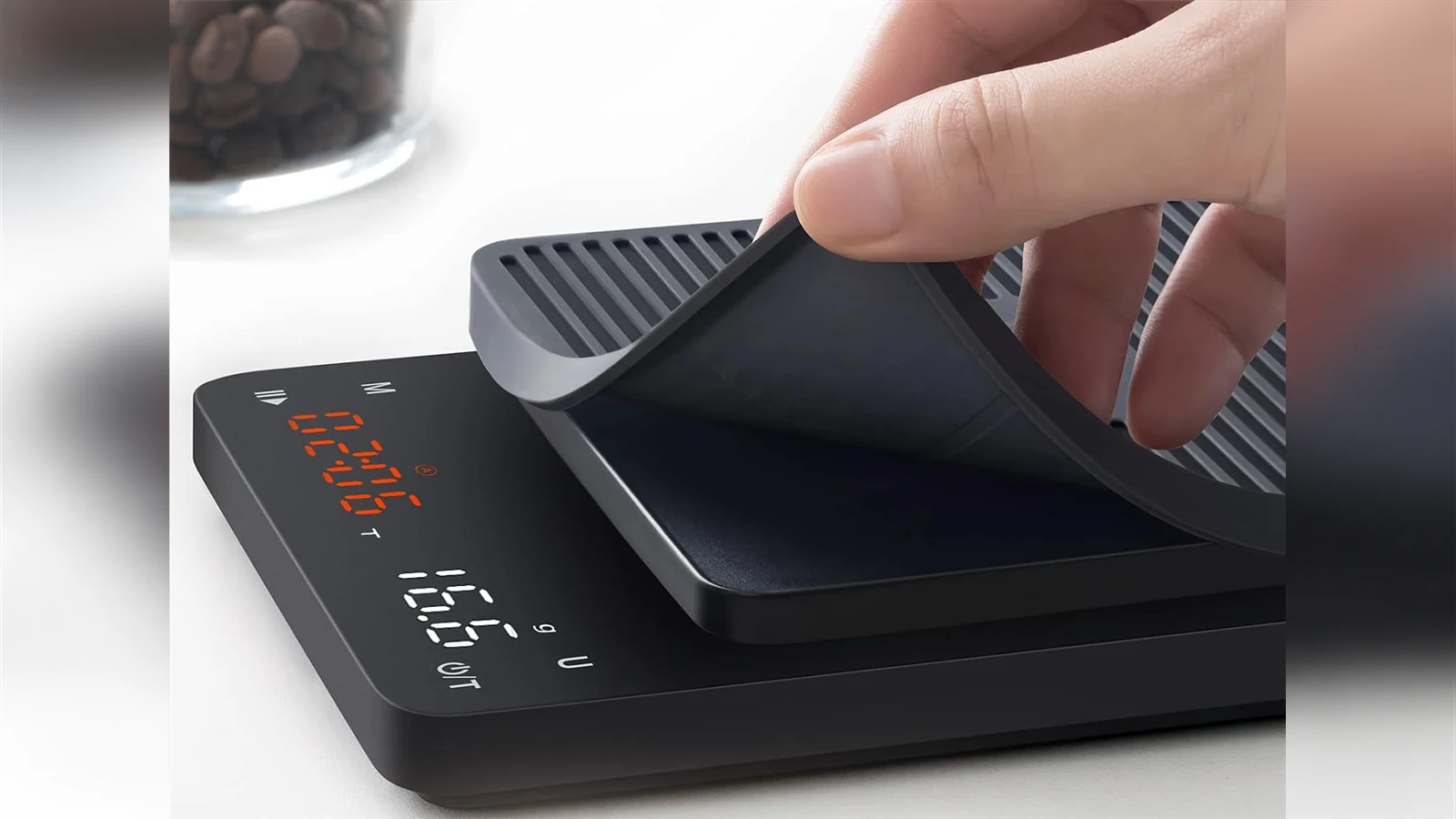 A hand lifting the removable silicone cover from a BAGAIL SC01 coffee scale