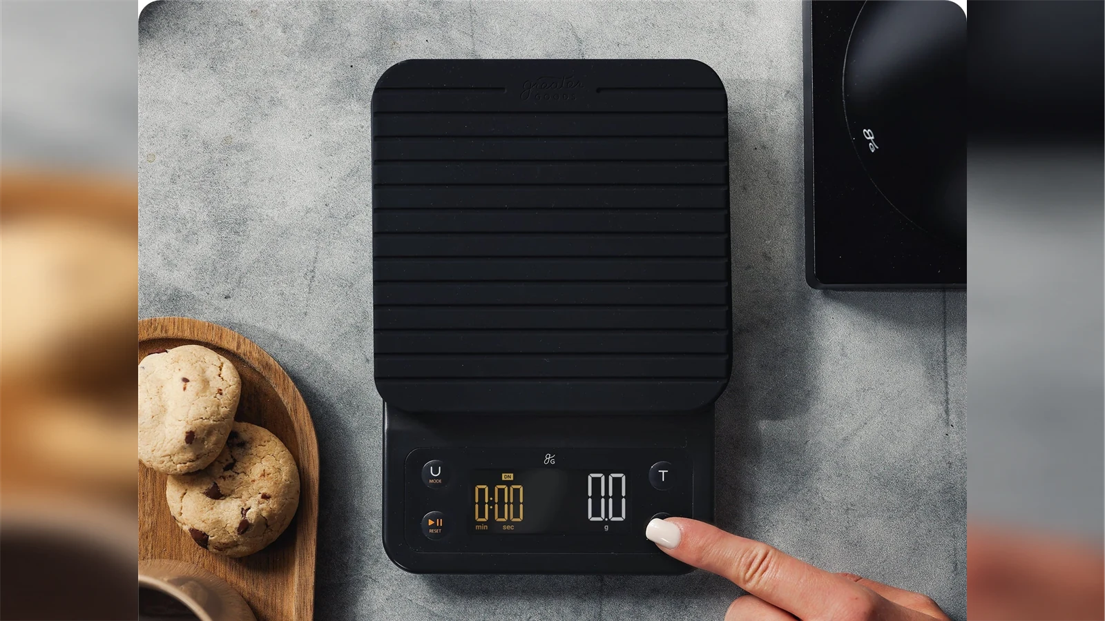 A hand pressing a physical button on the Greater Goods Premium 0460 coffee scale