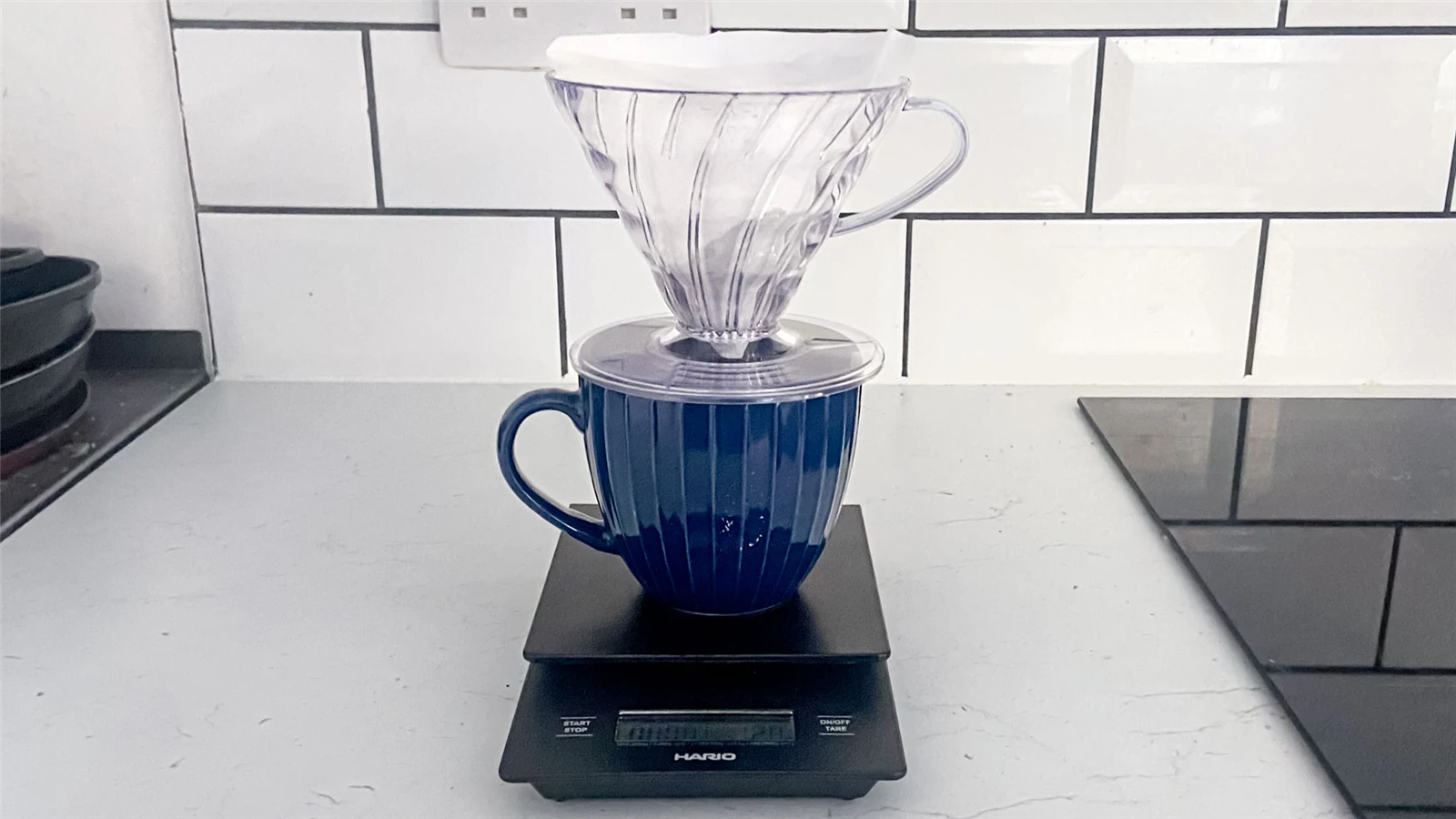 A Hario V60 dripper and blue mug standing on a Hario Drip Scale on a kitchen counter