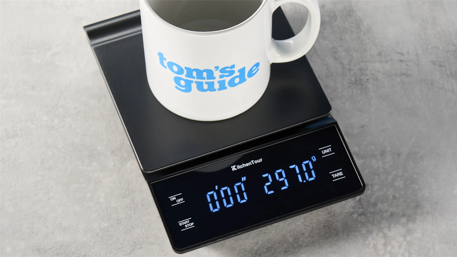 A white mug resting on a KitchenTour coffee scale on a counter