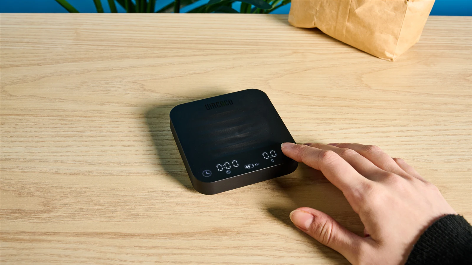 A hand using the WACACO Exagram Pro coffee scale on a wooden counter