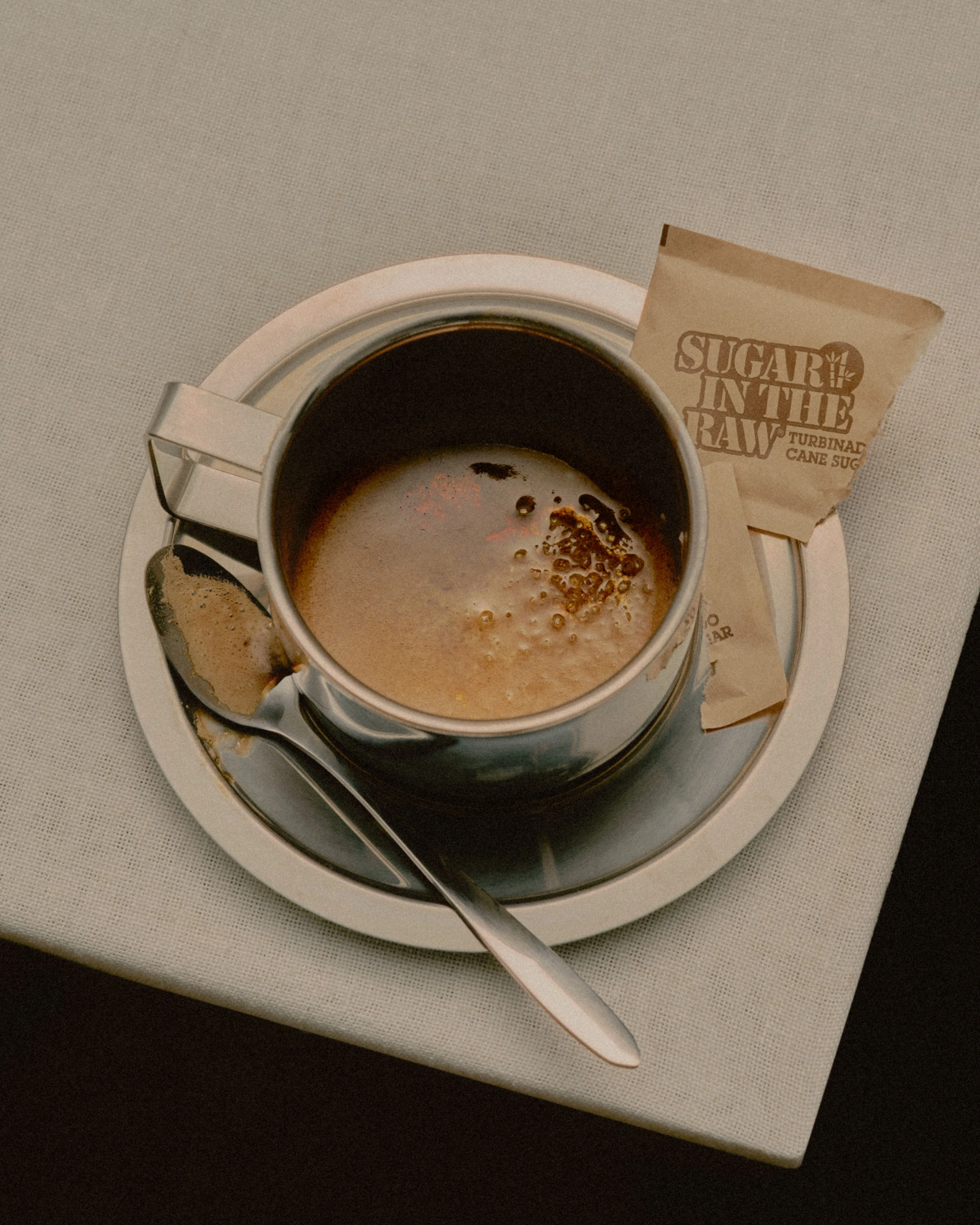 A cup of coffee on a saucer with a spoon and Sugar In The Raw packets