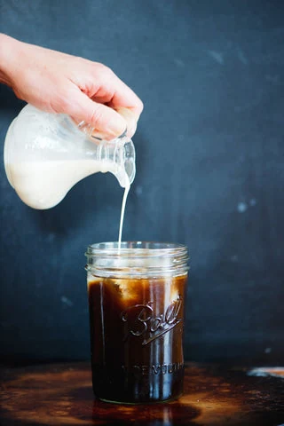 Cream being poured into a glass of iced coffee