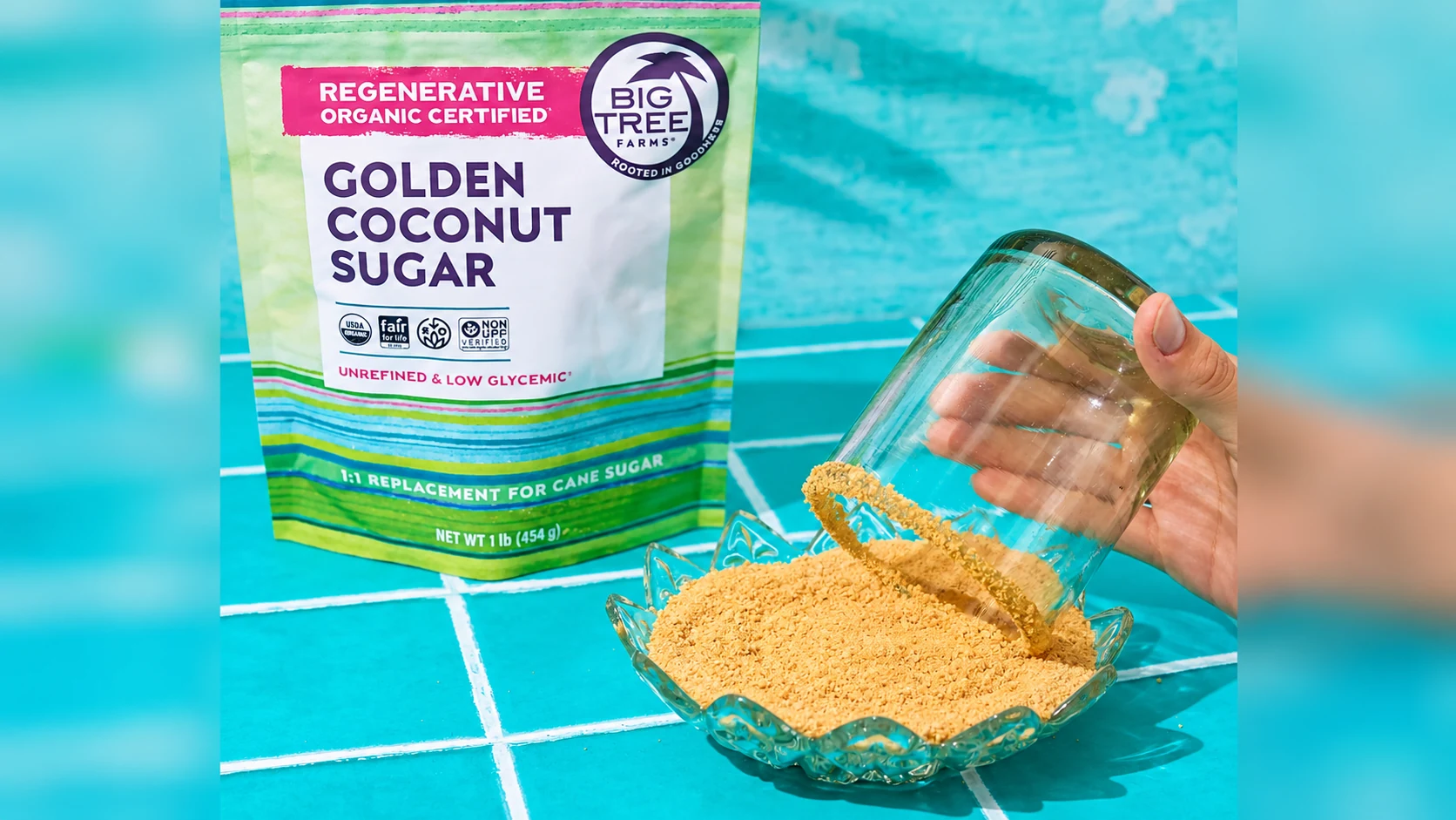 A hand tipping loose coconut sugar from a jar into a bowl beside Big Tree Farms Golden coconut sugar