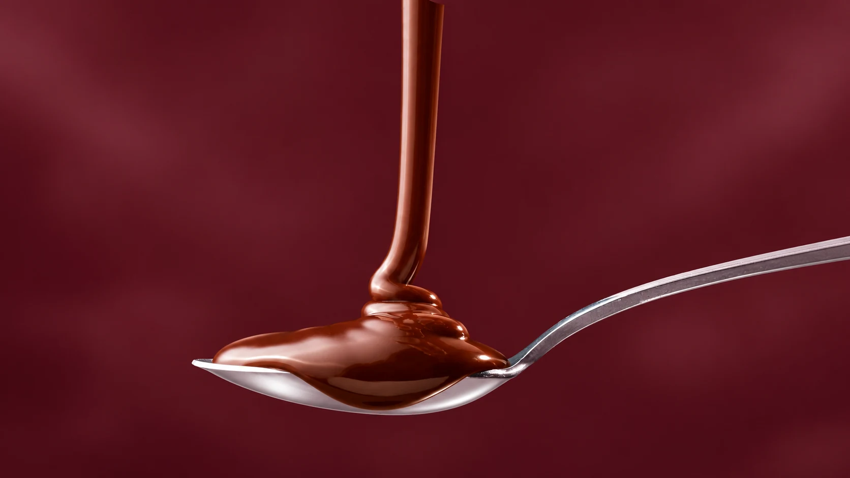 Chocolate syrup poured onto a spoon makes a measured dose visible before it goes into the coffee.