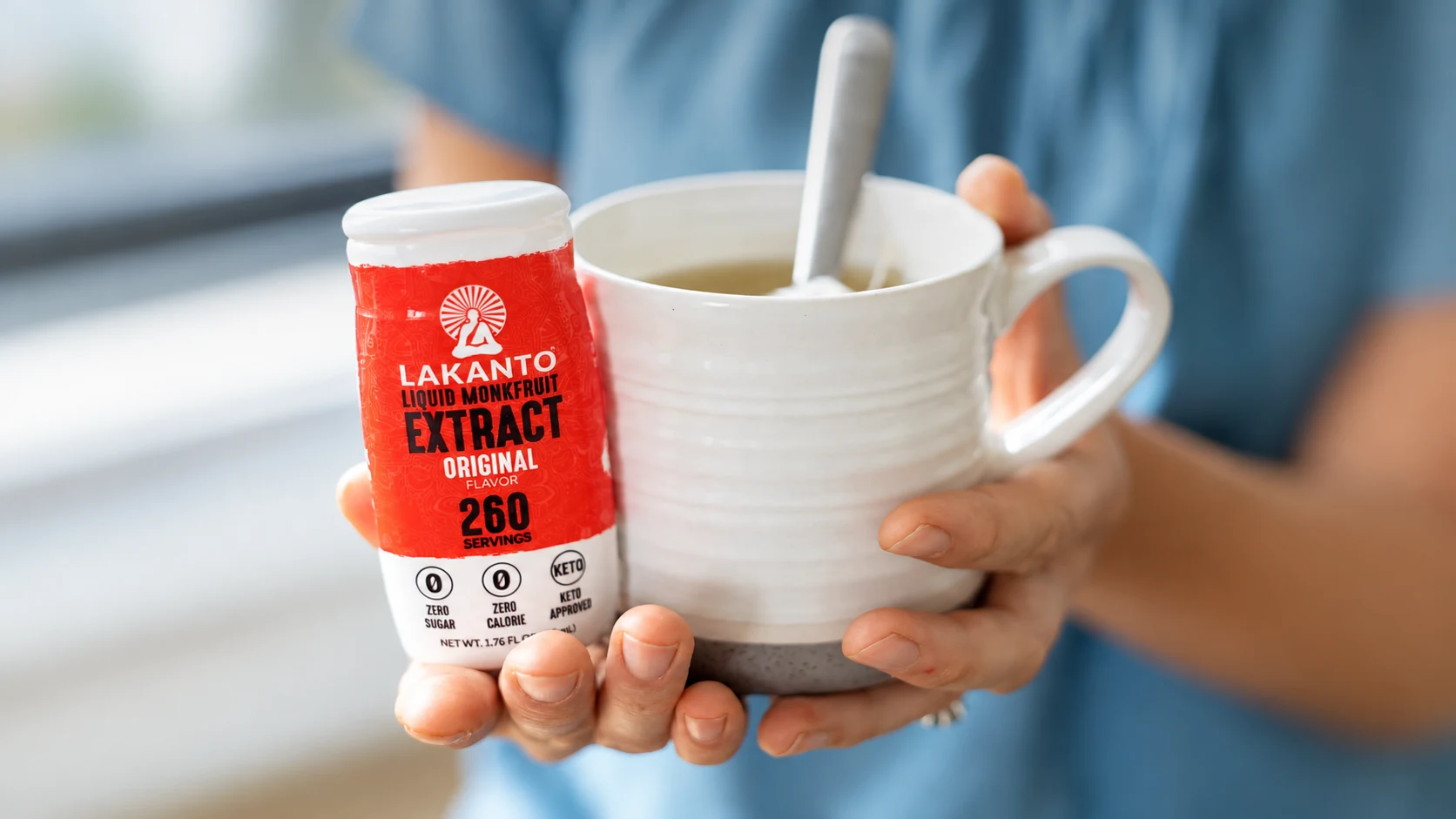 Hands holding Lakanto Original liquid monk fruit beside a white mug