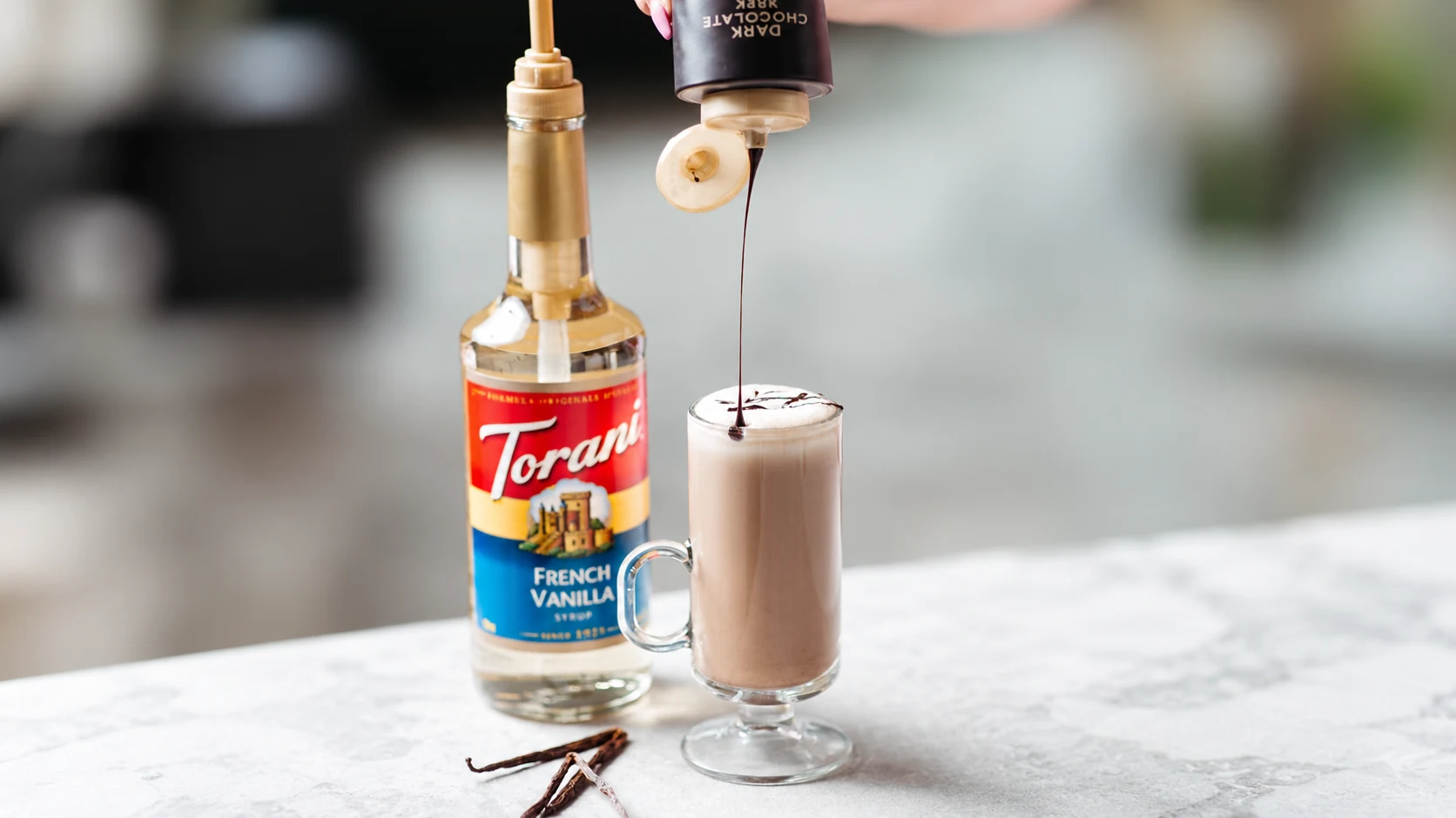French Vanilla syrup beside hot chocolate, with a separate chocolate sauce being added. This is a milk-drink serving example.