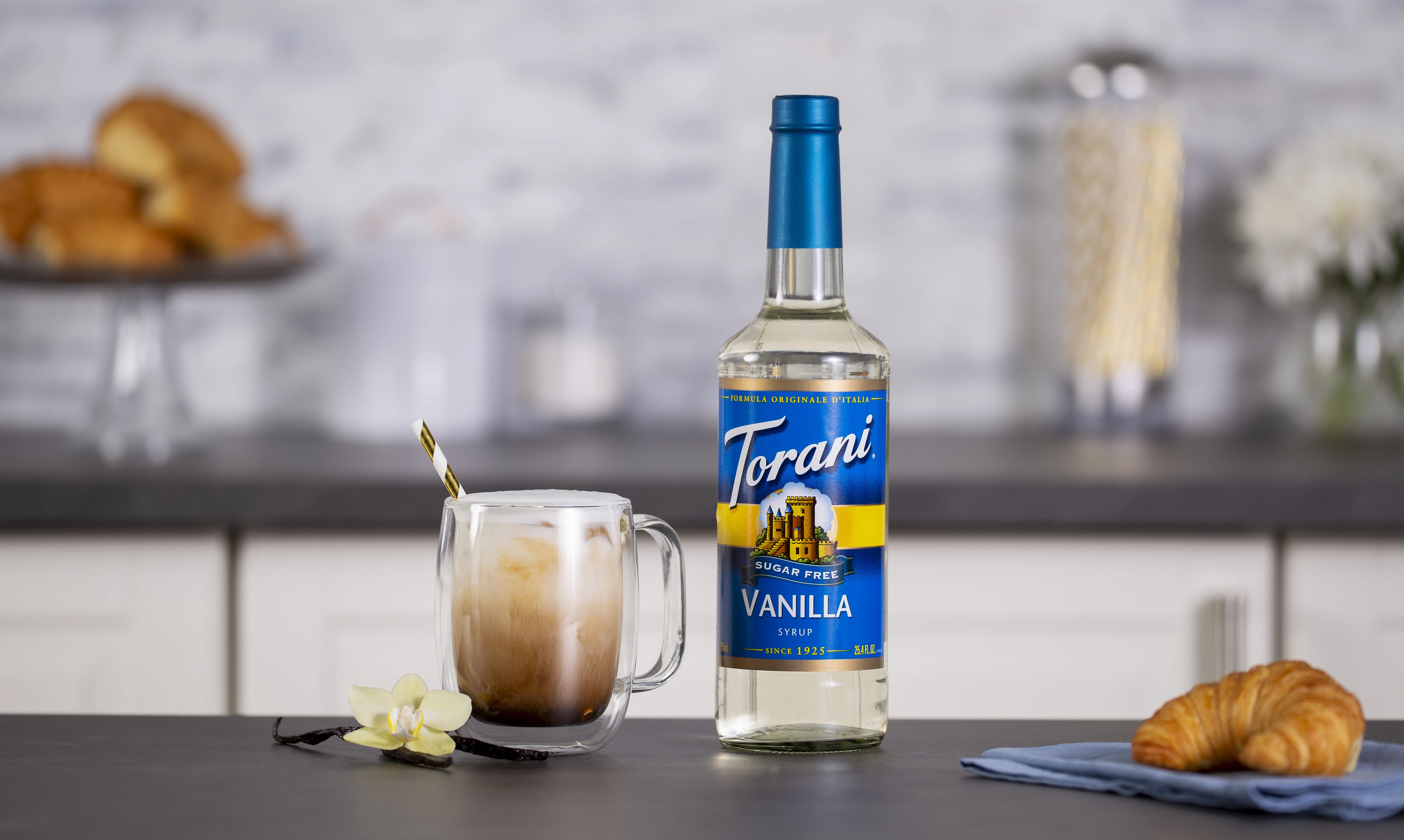 Torani Sugar Free Vanilla syrup beside an iced latte on a kitchen counter
