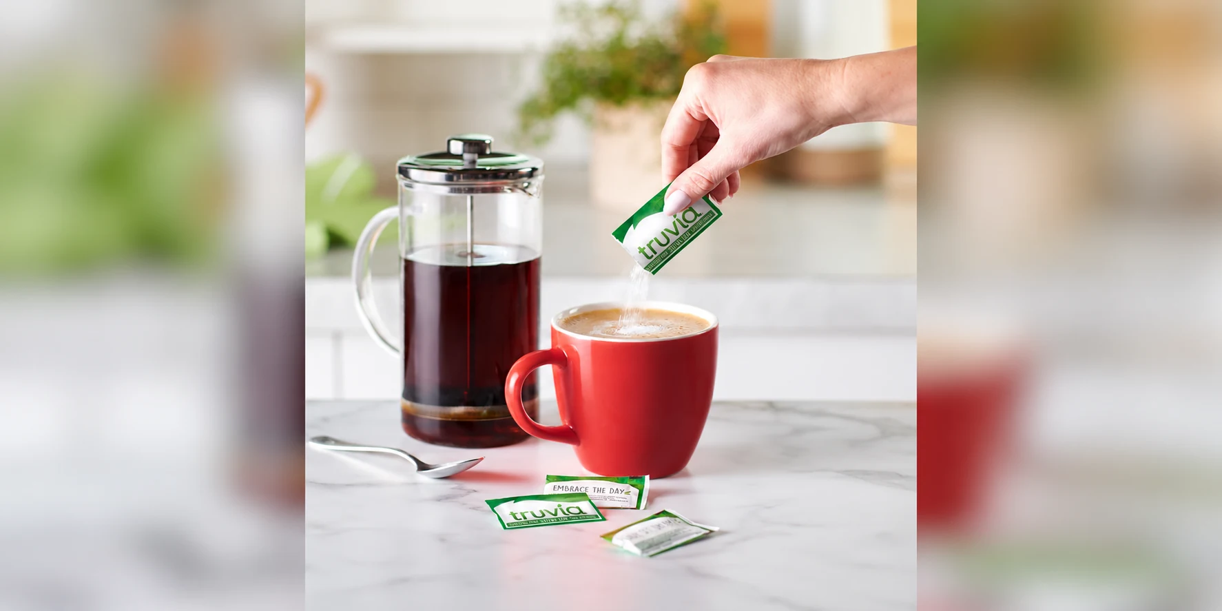 A hand pouring Truvia stevia sweetener from a packet into a red coffee mug