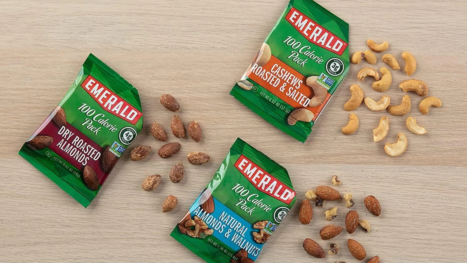 Three Emerald nut pouches with almonds and cashews arranged around them