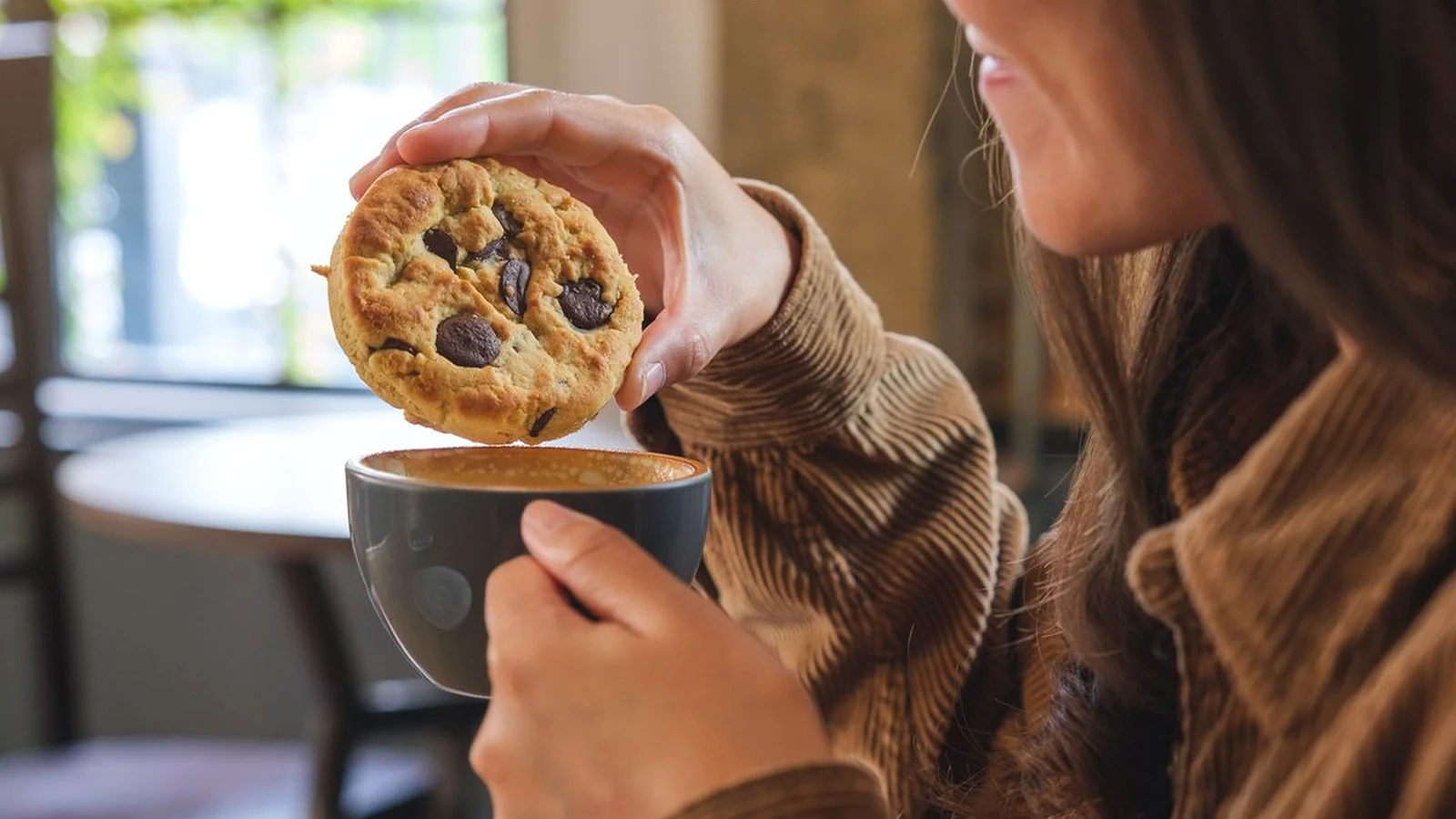 A chocolate chip cookie being dipped into a mug of coffee