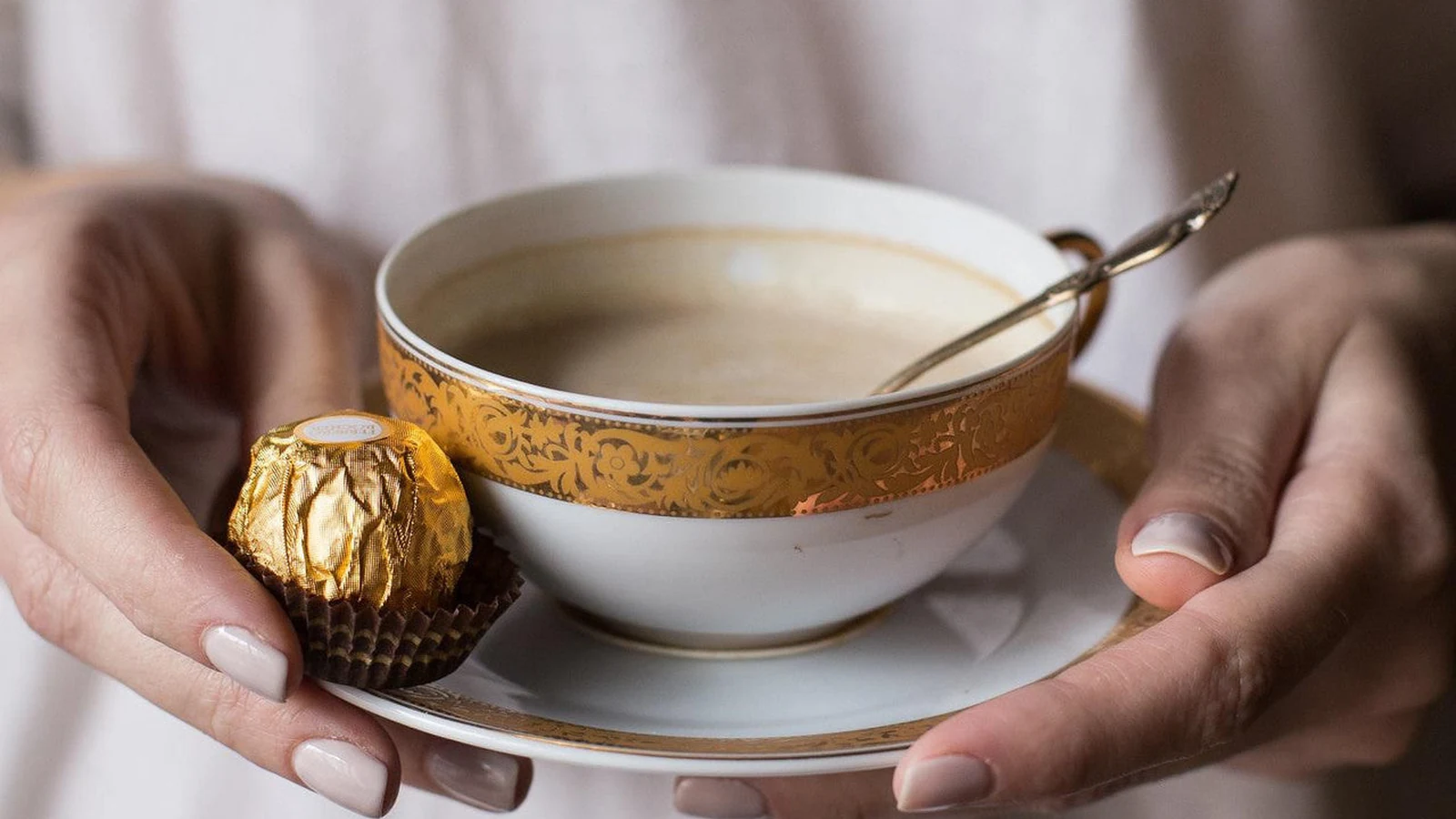 A gold-wrapped Ferrero Rocher on a saucer beside coffee