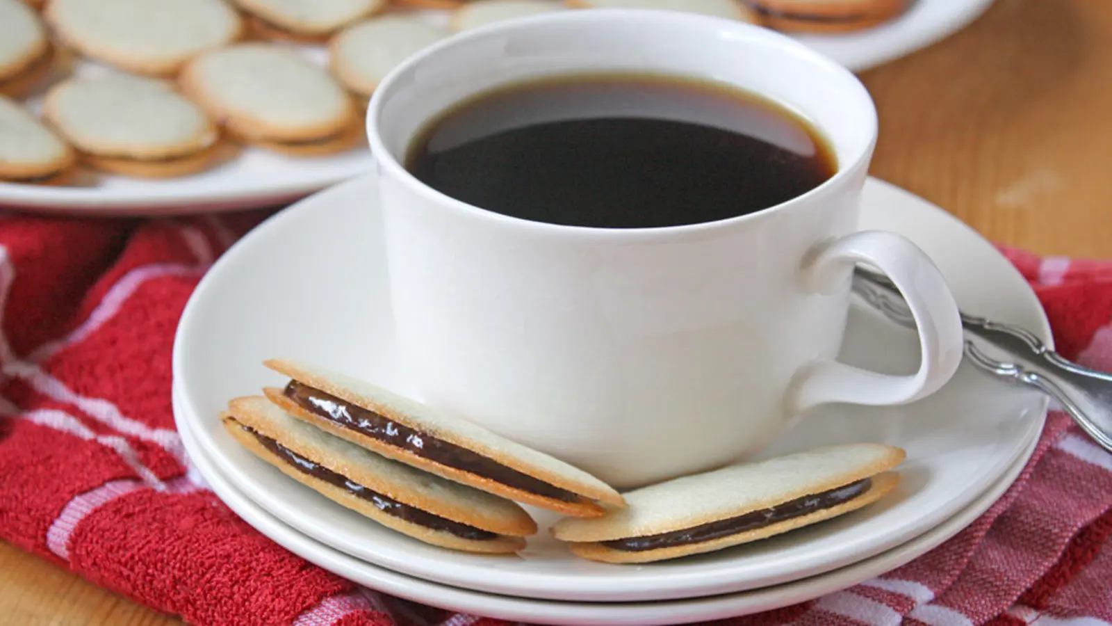 Oval chocolate sandwich cookies beside a cup of coffee