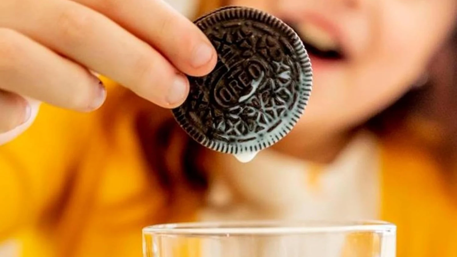 An OREO cookie held above a glass of milk