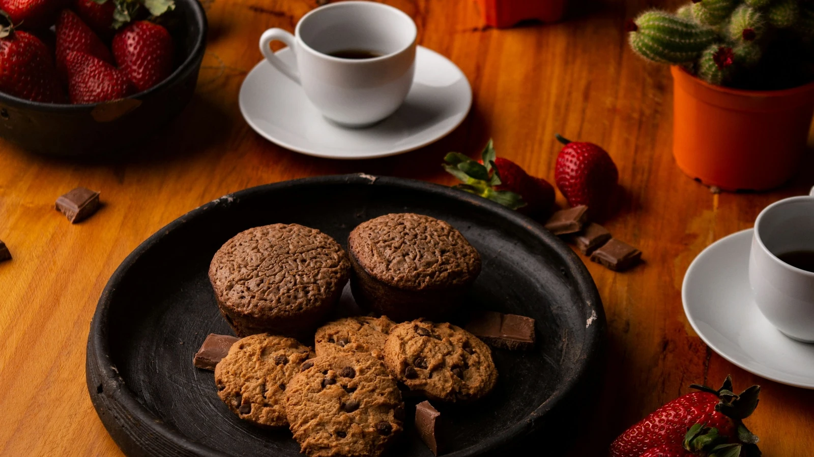 Coffee and assorted cookies on a wooden table with strawberries nearby; photo by Cindy Fernandez