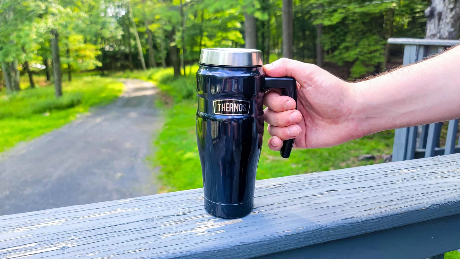 Black THERMOS Stainless King 16 oz travel mug held outdoors by its handle