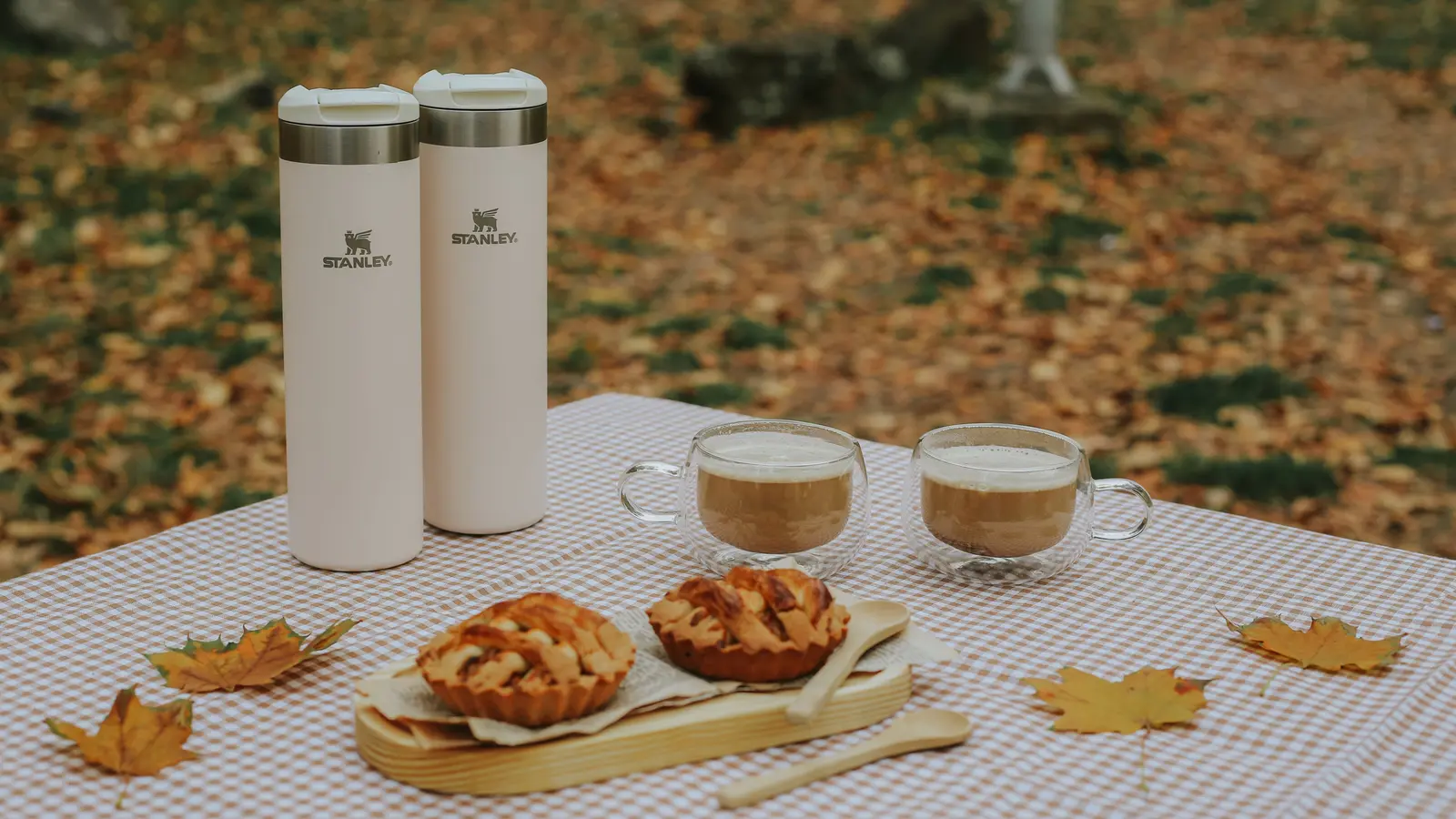 Stanley travel mugs beside two cups of coffee on an autumn picnic table