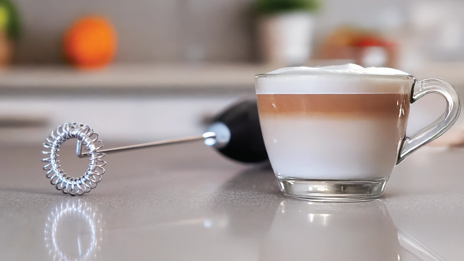 Black Elementi milk frother lying beside a glass latte