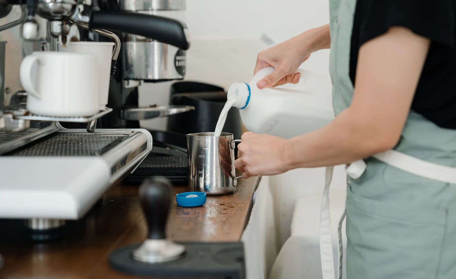 Barista pouring cold milk into a stainless steel pitcher. Photo: Ketut Subiyanto / Pexels.