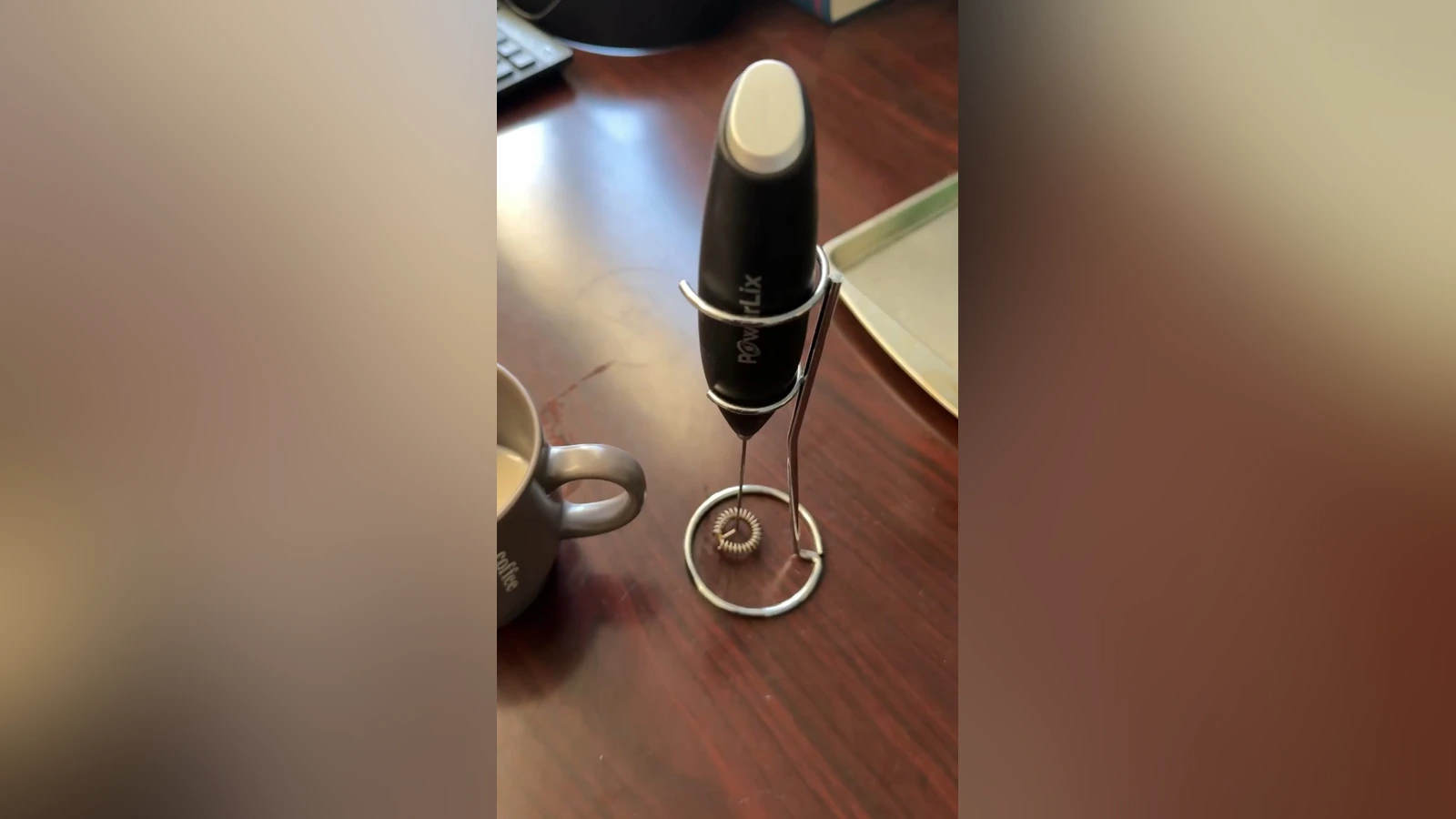 Black PowerLix frother on its wire stand beside a mug