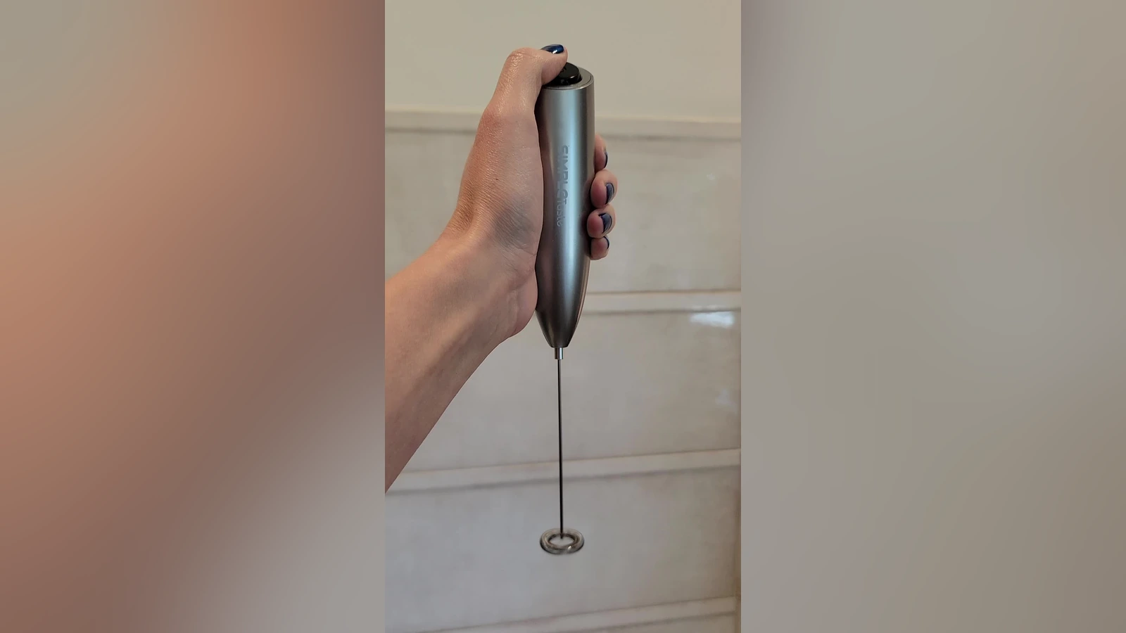 Silver SIMPLETASTE handheld frother held above a kitchen counter