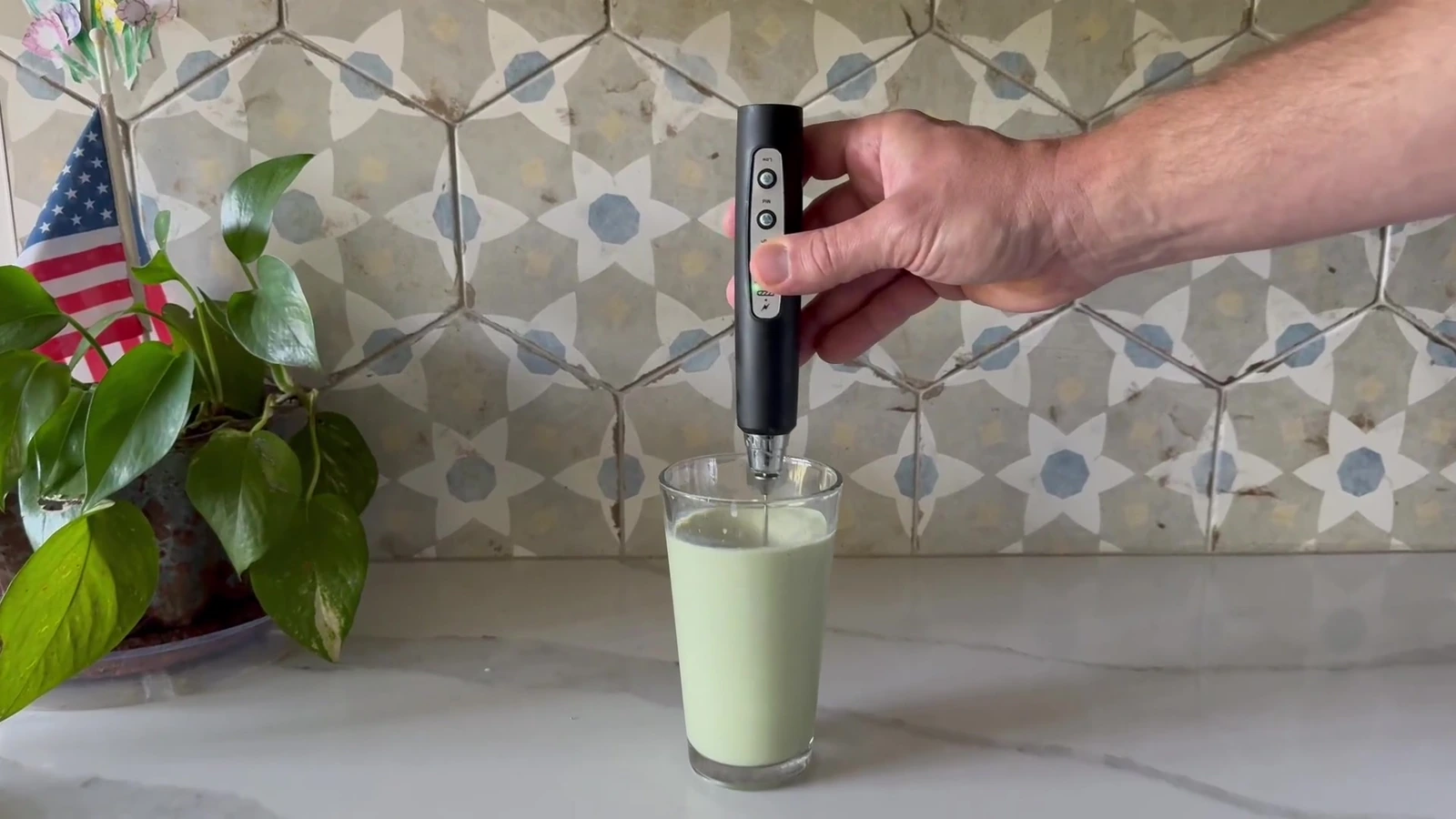 Black YUSWKO three-speed frother mixing a drink in a tall glass