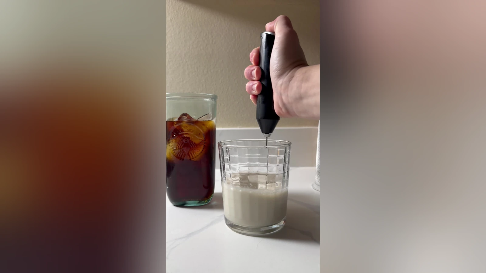 Black Zulay FrothMate frothing milk in a glass beside iced coffee