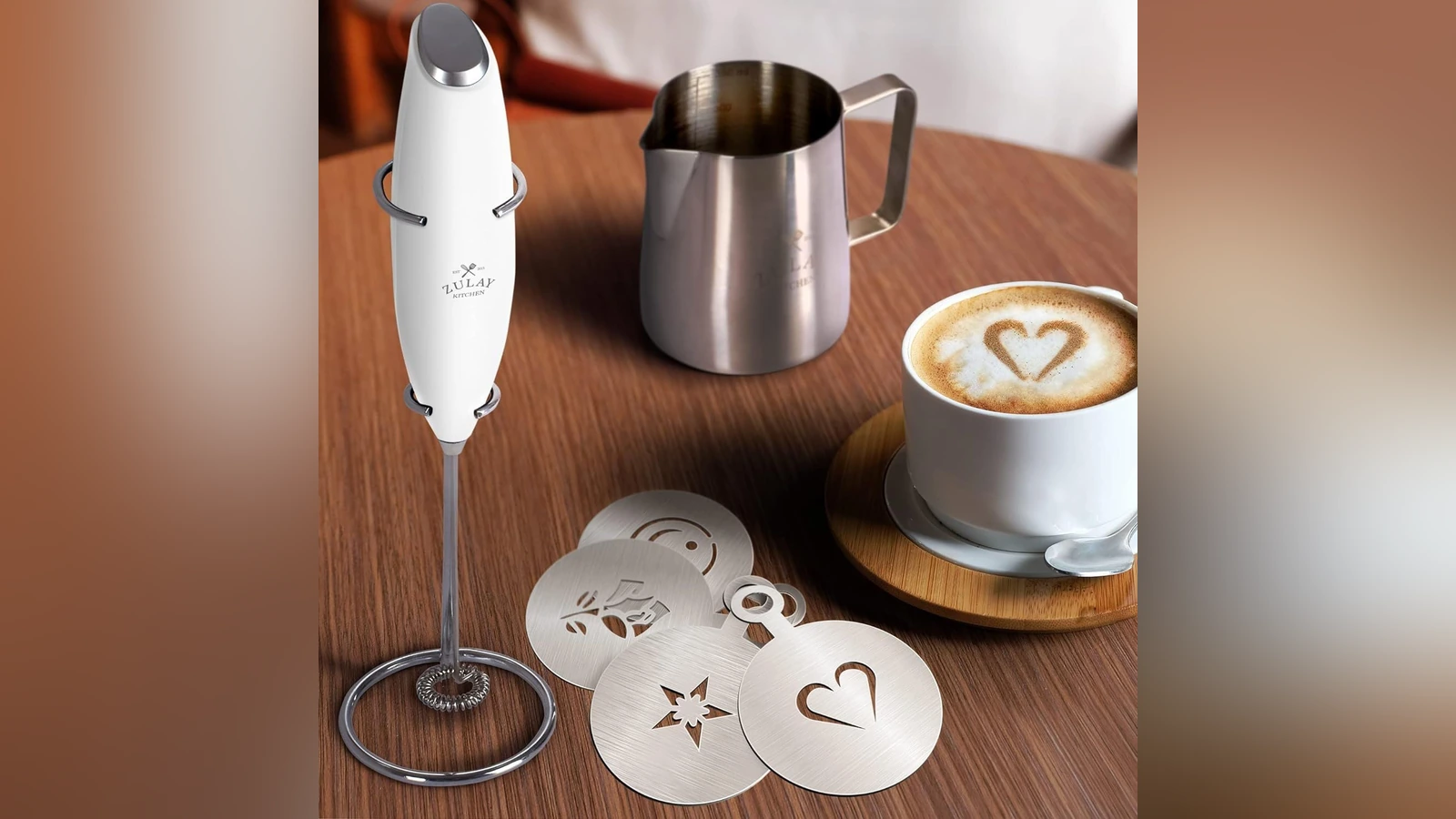 White Zulay frother on its stand with a stainless steel pitcher and four decorating stencils