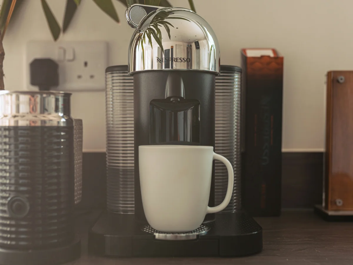 A chrome Nespresso machine and a white mug on a kitchen counter; photo by Studio 74