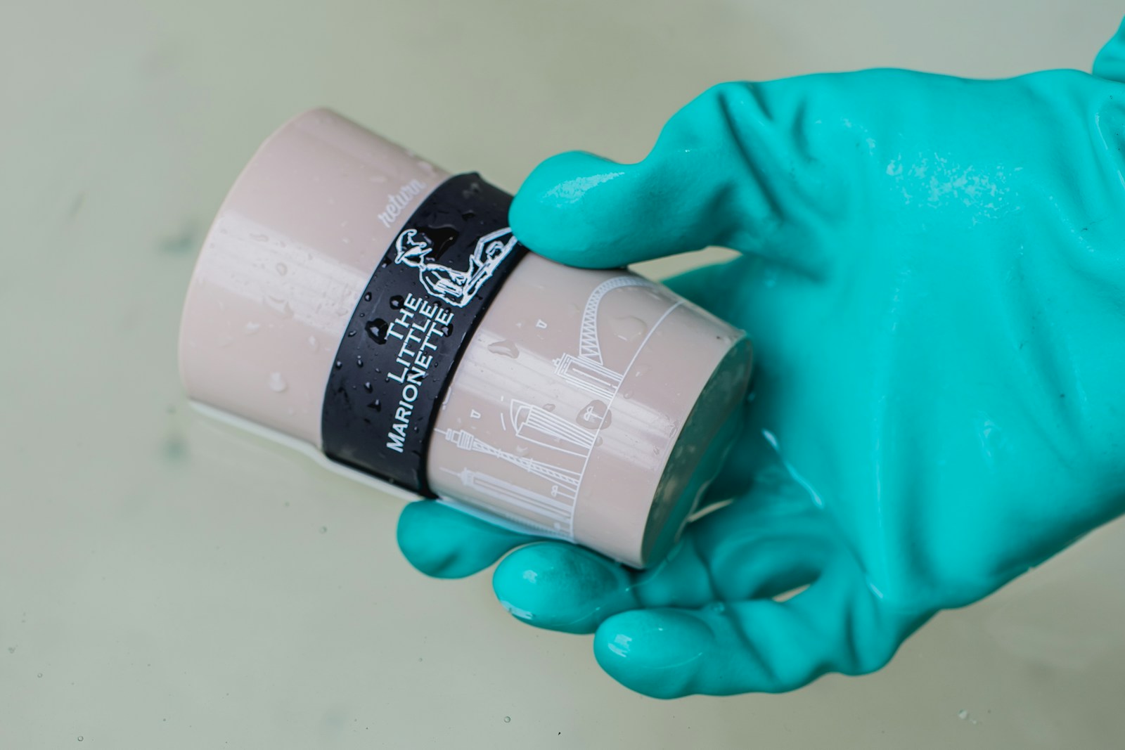 A gloved hand holding a wet reusable coffee cup with its lid removed