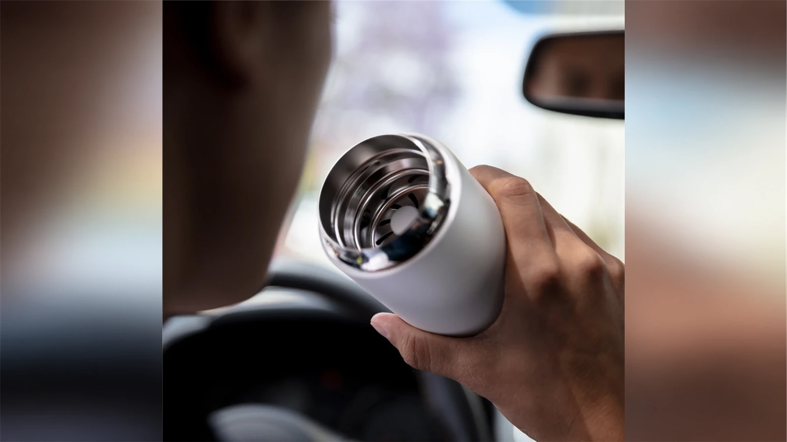 A hand holding an open Fellow Carter Move Mug in a car