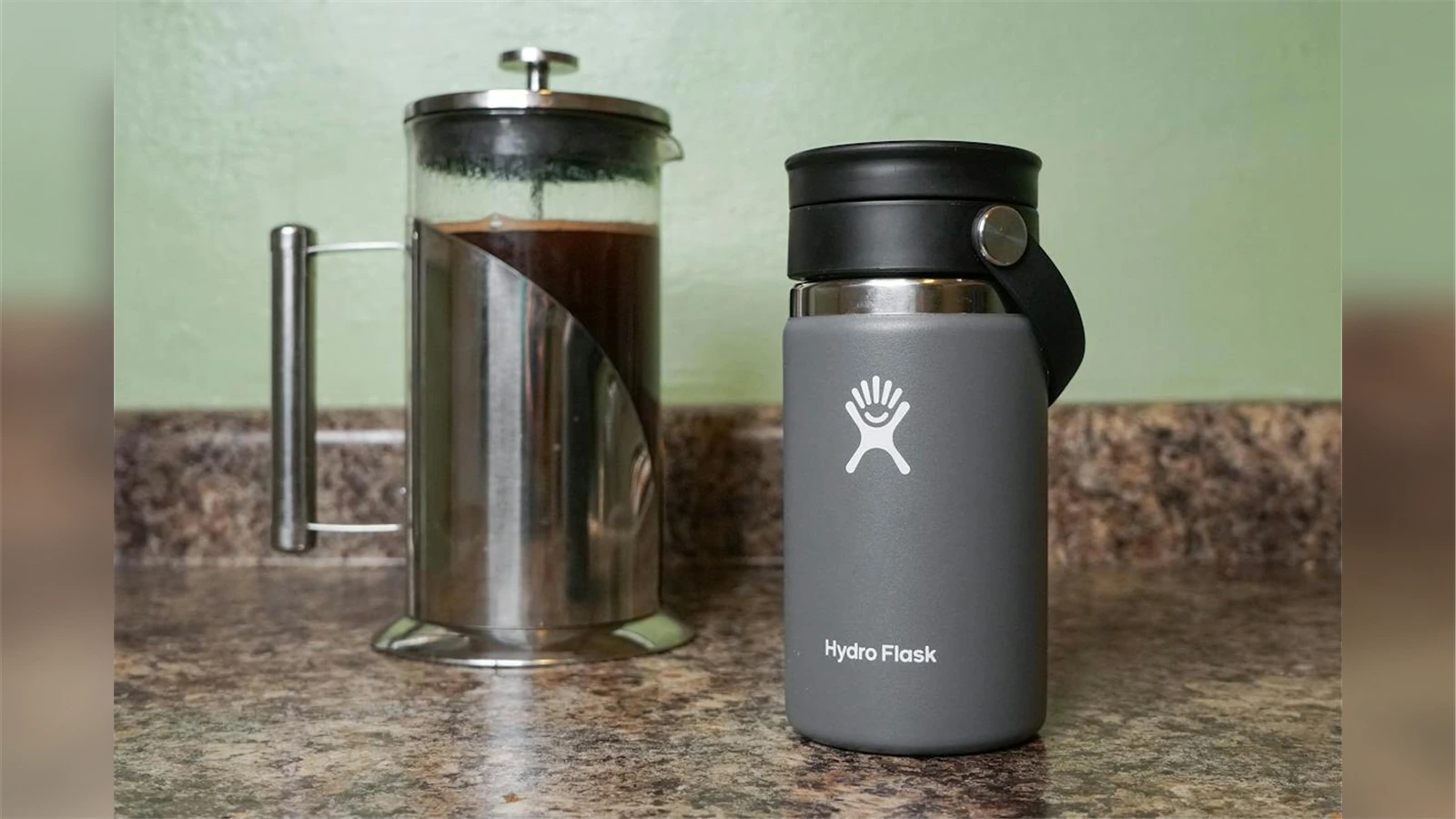 A grey Hydro Flask 12 oz bottle with its Flex Sip lid beside a French press