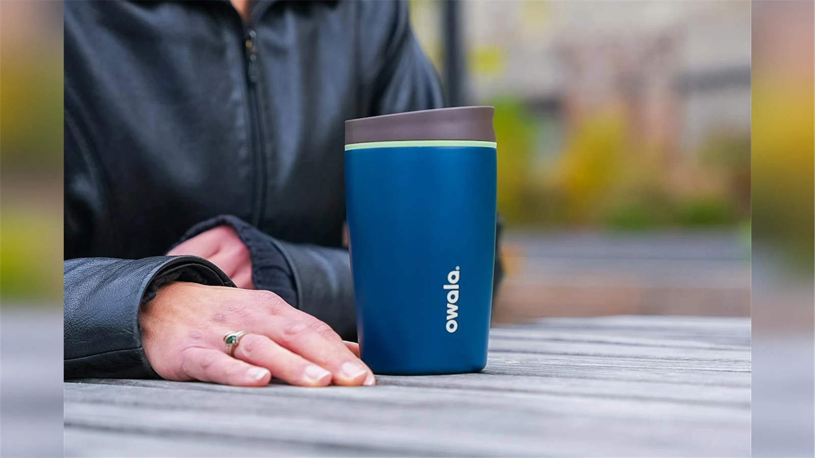 A blue Owala SmoothSip Slider 12 oz cup beside a hand on an outdoor table