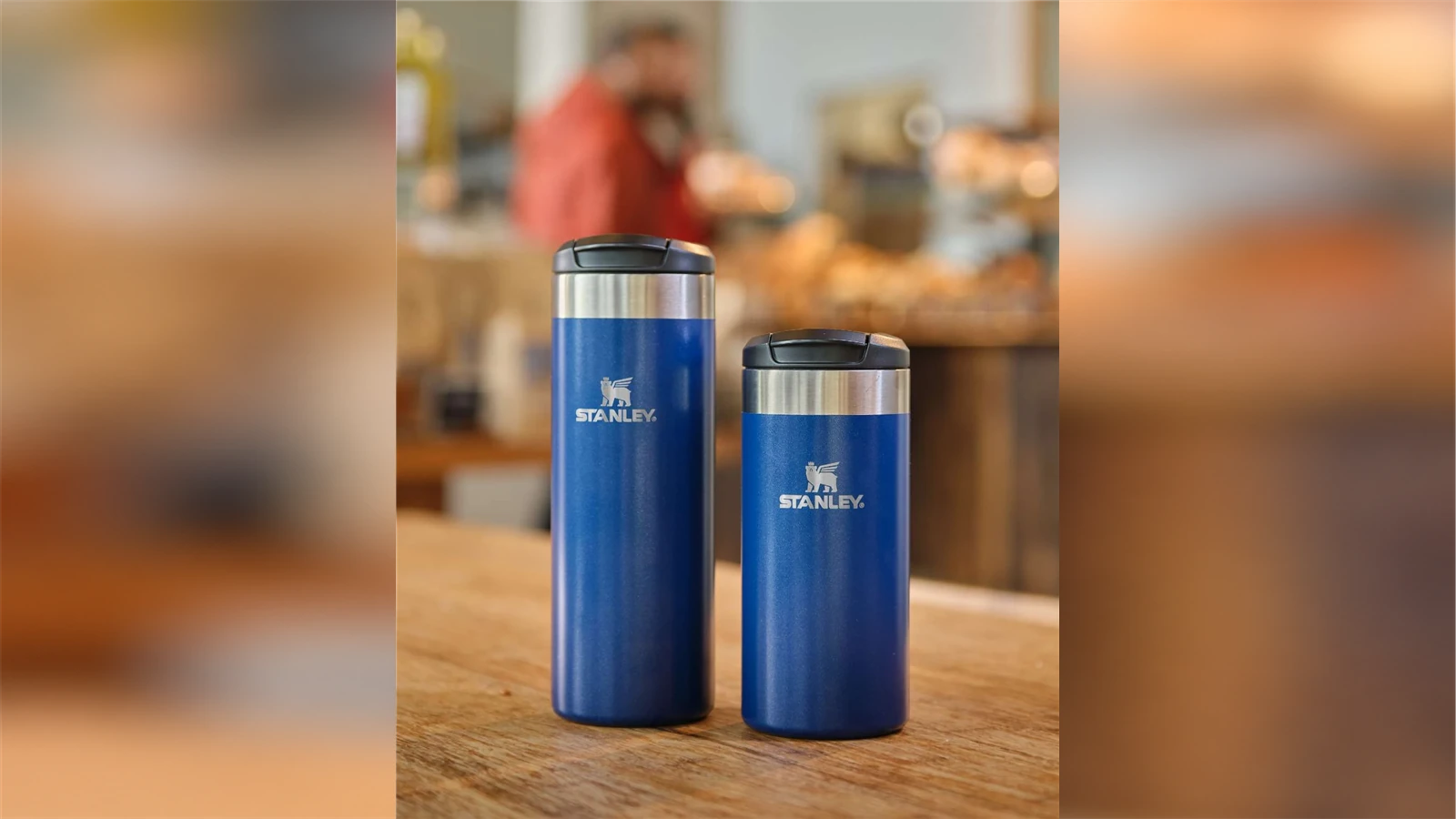 Blue Stanley AeroLight Transit mugs in 16 oz and 12 oz sizes on a cafe table