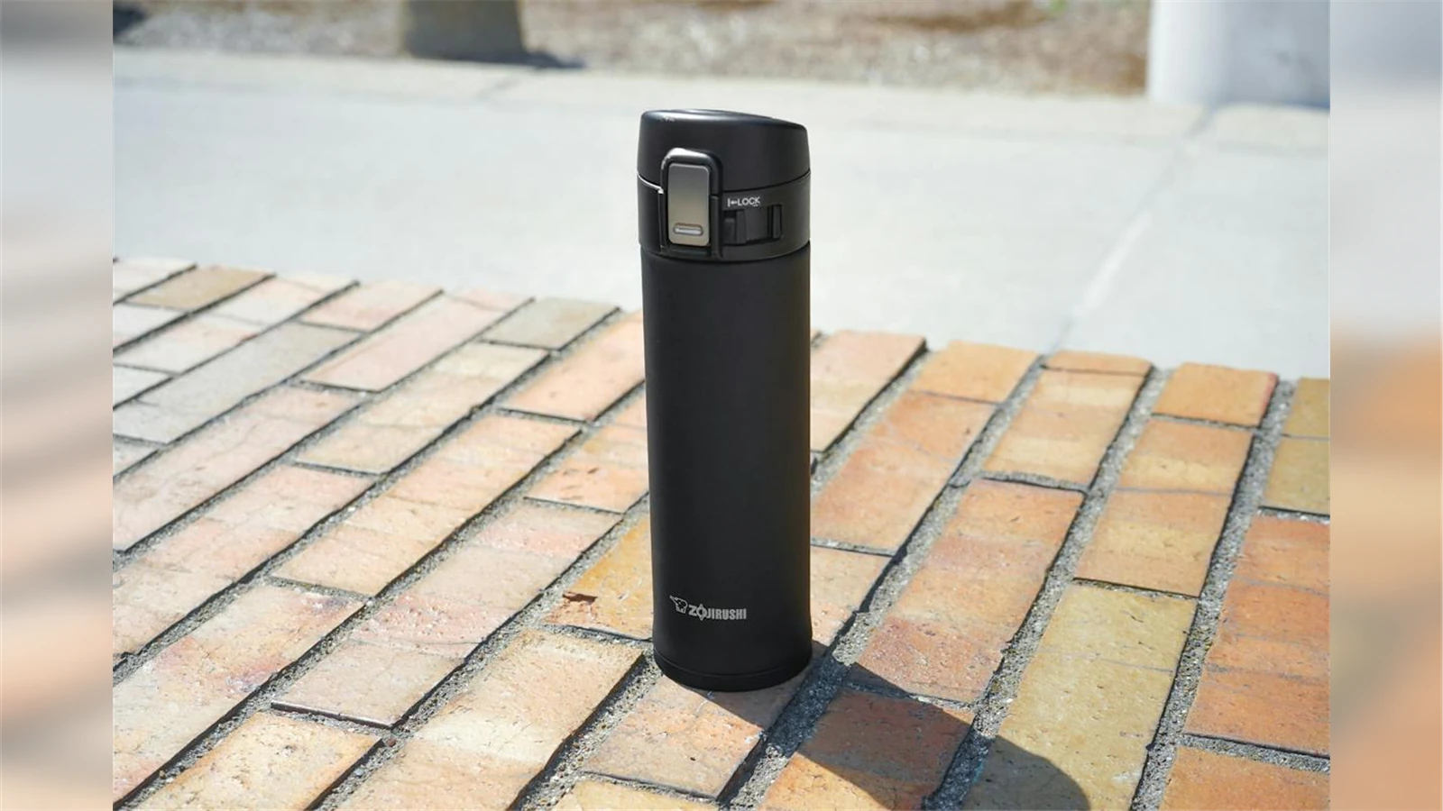 A black Zojirushi SM-KHE48 16 oz mug with its locking flip lid on an outdoor brick table