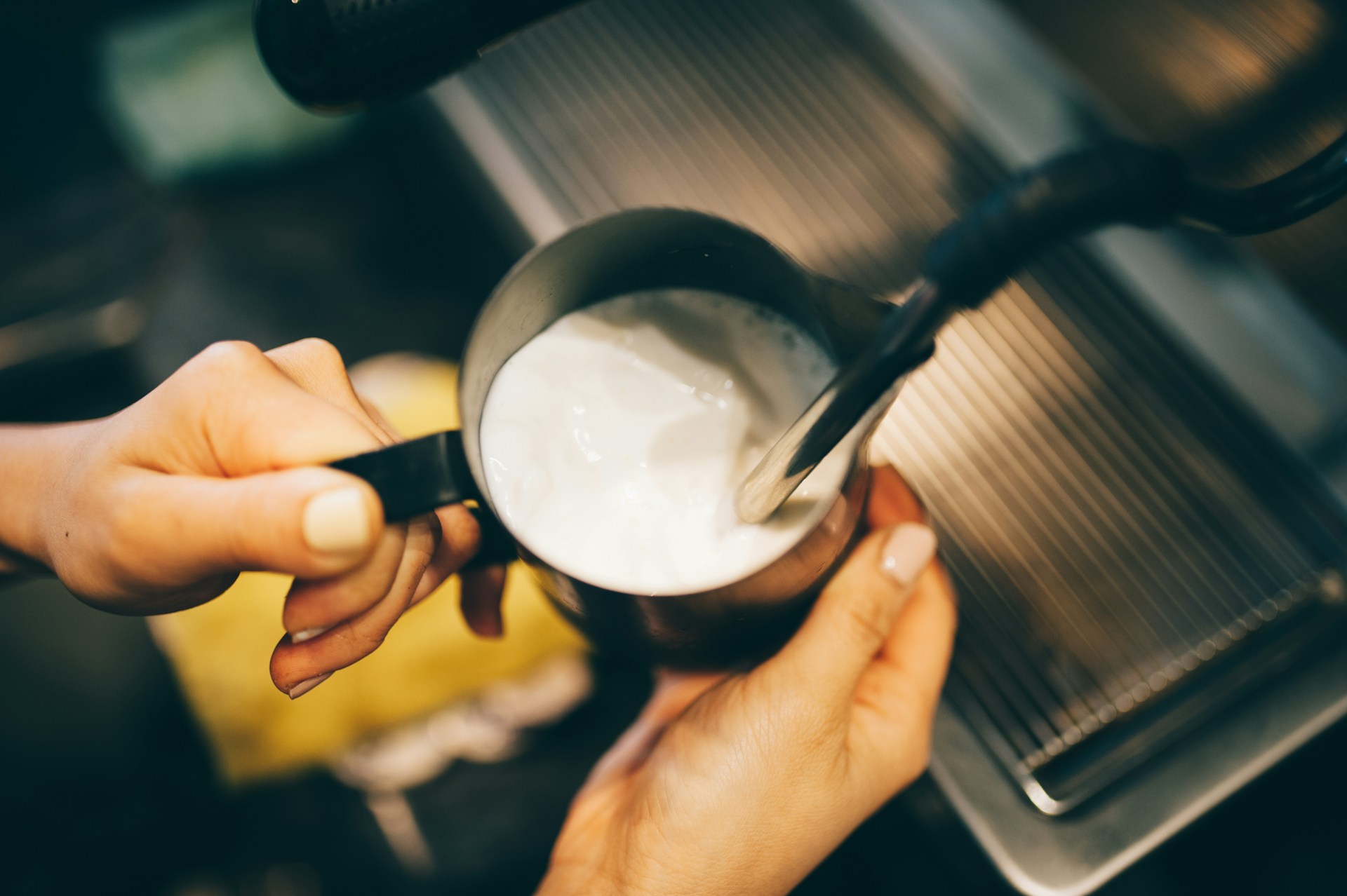 Barista steaming milk in a stainless steel pitcher using an espresso machine steam wand