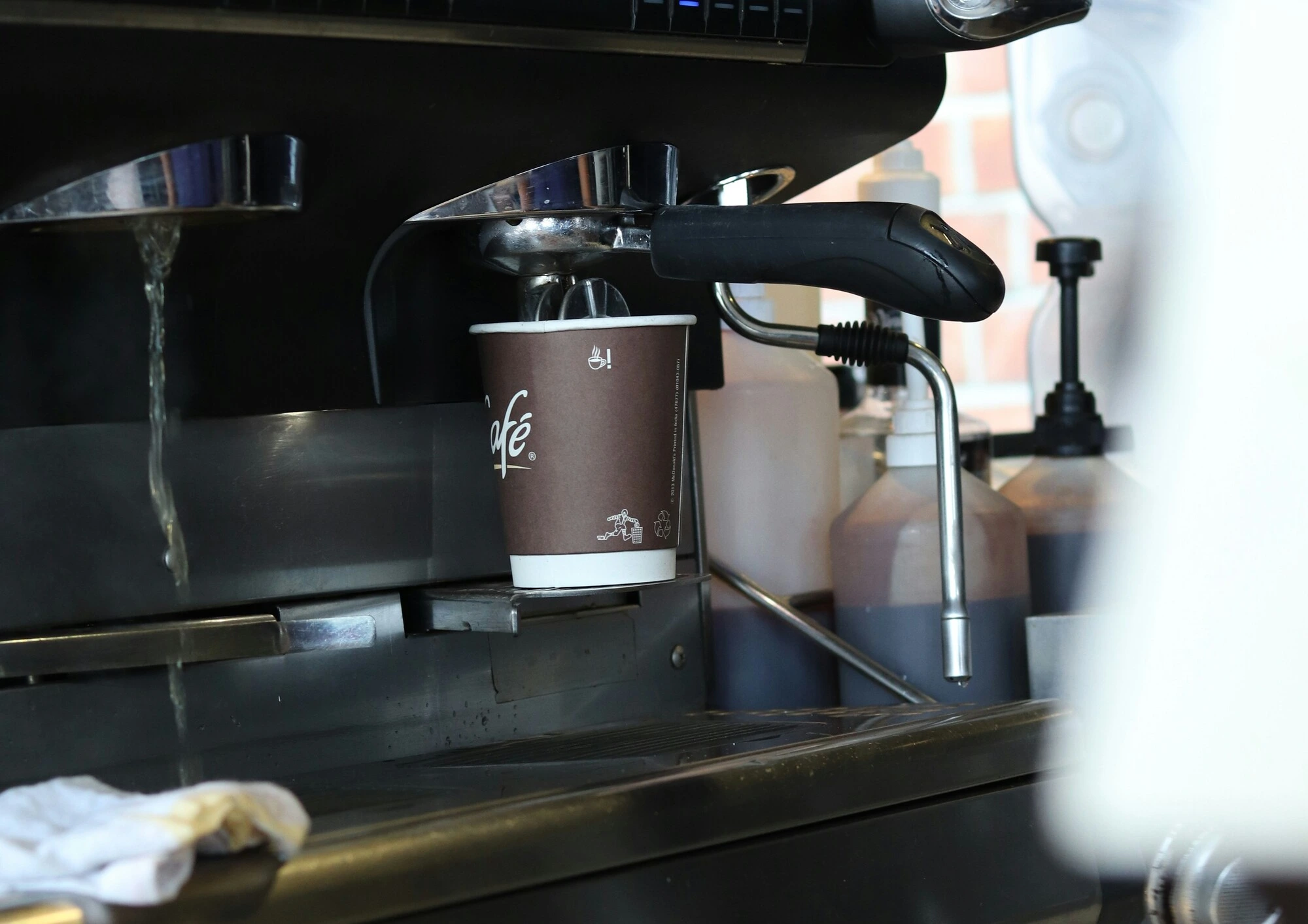 Espresso machine flushing hot water through the group head into a paper cup