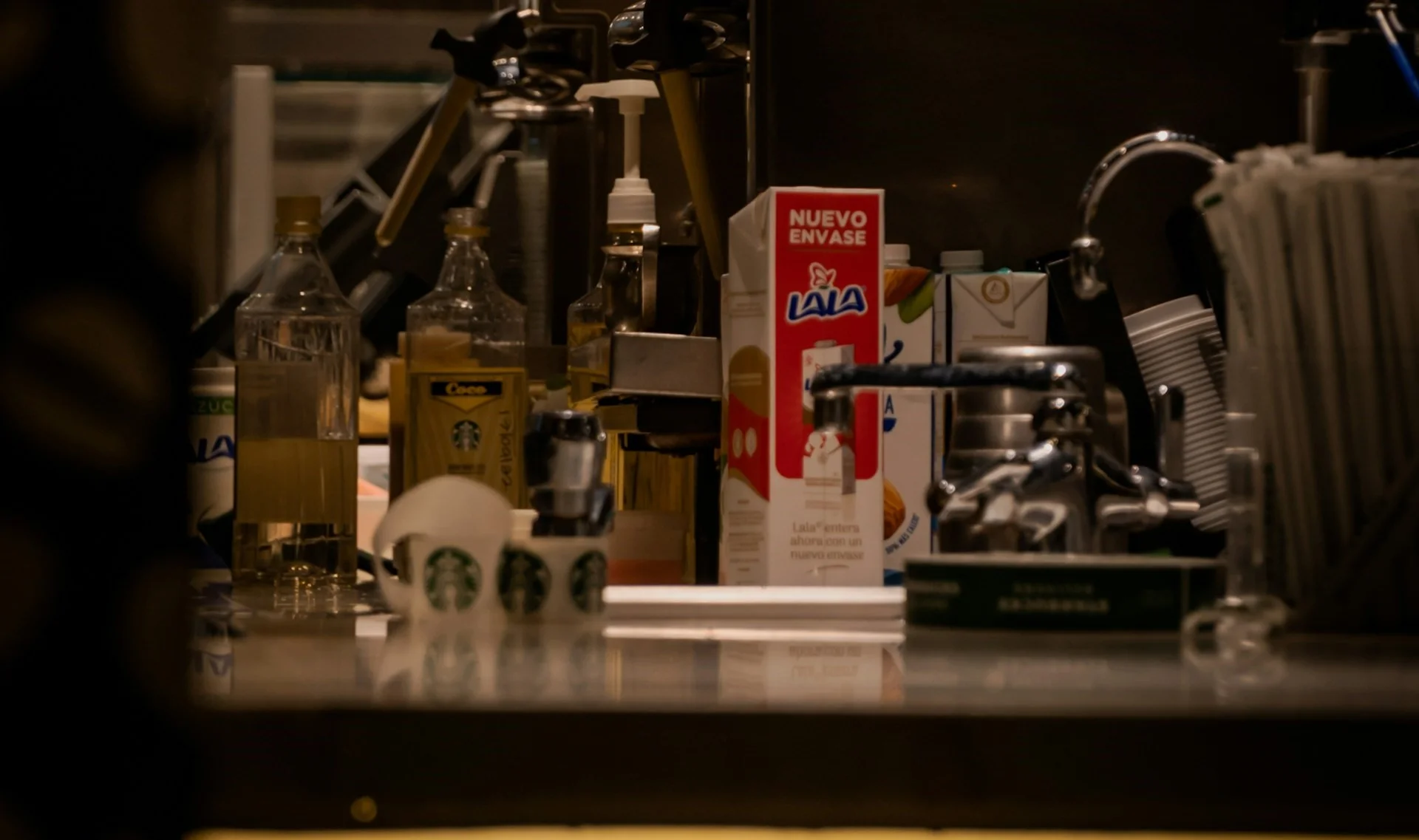 Different kinds of milk and plant-based alternatives in glass bottles on a counter next to an espresso machine